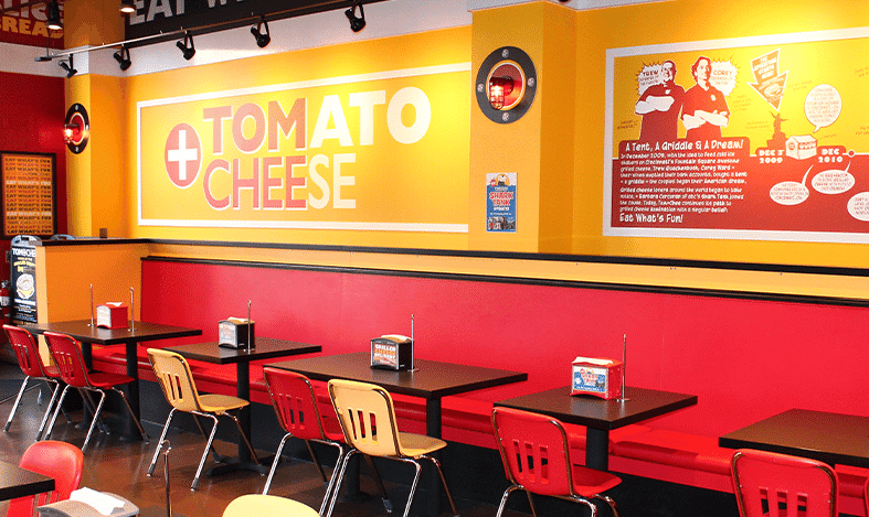 chairs at tables and a large wall sign tom + chee